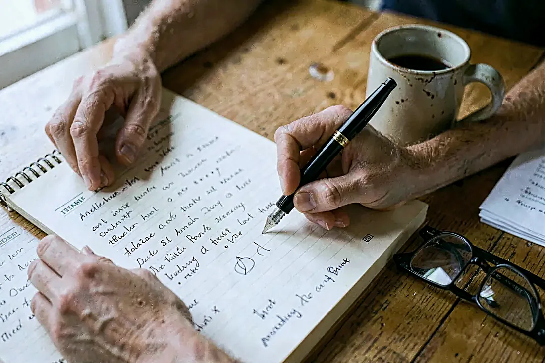 Des mains d'adulte remplissent à la main un registre d'appel en papier, posé sur une table en bois.